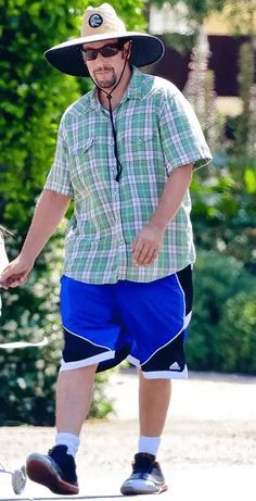 a man in a hat and blue shorts is walking his dog