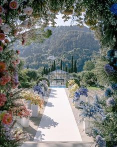 an outdoor ceremony with flowers and greenery on either side of the aisle, surrounded by trees