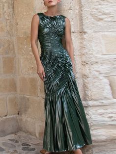 a woman standing in front of a stone wall wearing a green dress with pleated details