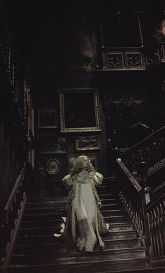 a woman is walking down the stairs in a dark room with white walls and wooden railings