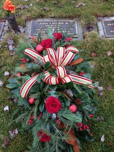 a wreath with red flowers and greenery on top of a grave in the grass