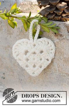 a white crocheted heart hanging on a stone wall next to a pine cone