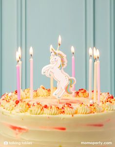 a birthday cake with white frosting and pink icing has unicorn candles on it