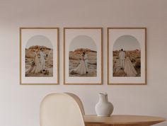 three framed pictures hang on the wall above a table with a vase and chair in front of it