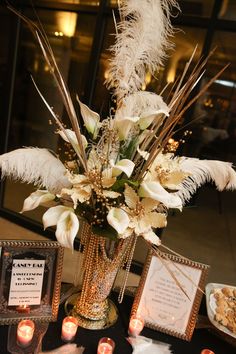 a vase filled with white flowers and feathers on top of a table next to candles