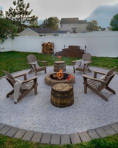 a fire pit with chairs around it in the middle of a backyard area that has grass and gravel on both sides