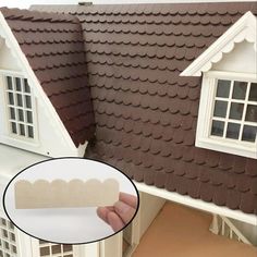 a hand holding up a fake house with windows and sidings on the side of it