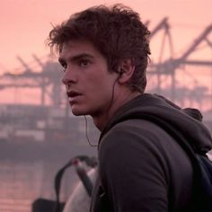 a young man with earphones standing in front of a body of water at sunset