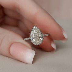 a woman's hand holding an engagement ring with a pear shaped diamond