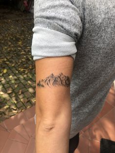 a person with a tattoo on their arm and mountains in the backgrouund