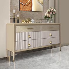 a white and gold dresser with vases on top of it next to a painting