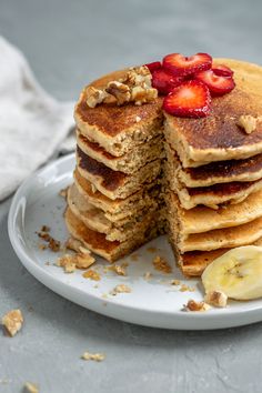 a stack of pancakes topped with sliced bananas and strawberries