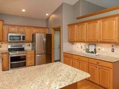 an empty kitchen with granite counter tops and stainless steel appliances in the center, along with light wood cabinets