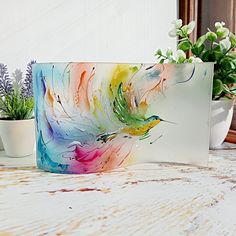 a colorful painting sitting on top of a wooden table next to a potted plant