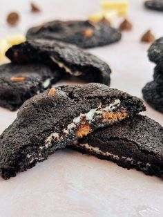 chocolate cookies with white and orange fillings on a table next to one cookie broken in half