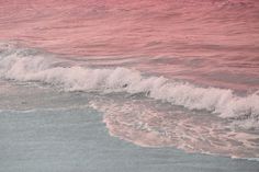 the water is pink and white as it comes in from the shore line to the beach