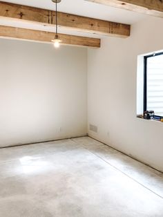 an empty room with white walls and wood beams on the ceiling is shown in front of a window