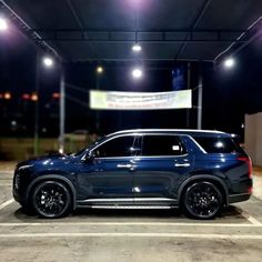 a blue suv parked in a parking lot at night with bright lights on the ceiling