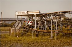 an abandoned gas station with a roller coaster in the foreground and buildings in the background