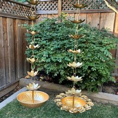 two metal bowls with water lilies hanging from them in the grass next to a wooden fence