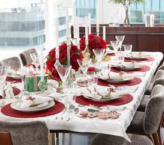 the table is set for christmas dinner with red flowers and silverware on it,