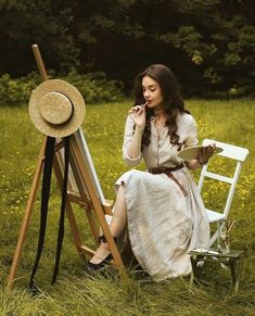 a woman sitting on a chair next to an easel