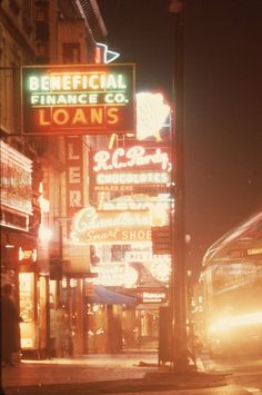 a city street at night with neon signs and buses on the side of the road