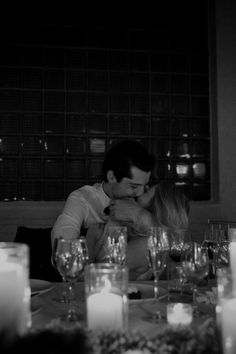 a man and woman kissing in front of candles at a table with wine glasses on it