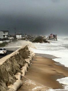 cars are driving on the road next to the ocean and houses with storm clouds in the background