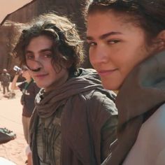 two young women standing next to each other in front of a desert area with people