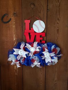 a baseball wreath with the word love is hanging on a wooden wall next to a red, white and blue bow