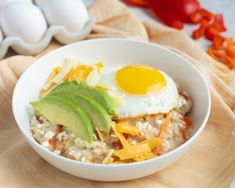 a white bowl filled with rice and topped with an egg, avocado and cheese