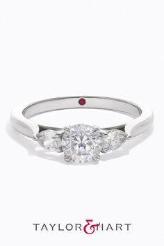 a three stone engagement ring with two diamonds on the side and a red diamond in the middle