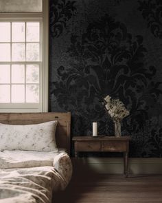 a bed sitting next to a window in a room with dark wallpaper and wooden flooring