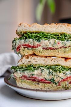 two sandwiches stacked on top of each other on a white plate with green and red toppings