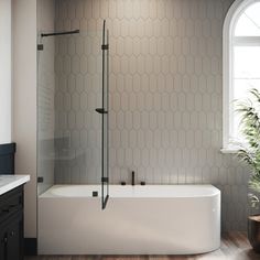 a white bath tub sitting under a window next to a potted plant on top of a wooden floor