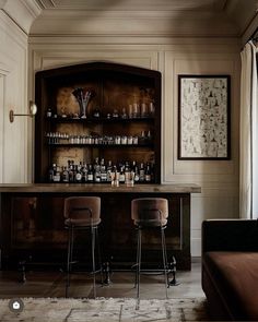 two bar stools sitting in front of a wooden cabinet filled with bottles and glasses