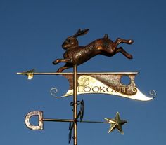 a weather vane with a rabbit on it and the word look out written in cursive letters