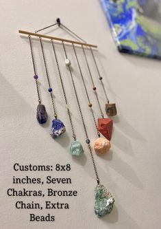 a group of different colored rocks hanging from a metal bar on a white wall next to a piece of paper