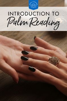 a woman's hands with black nail polish and gold ring on her finger, in front of a wooden table