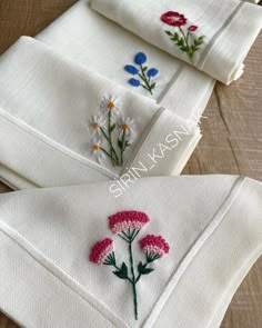 four embroidered napkins with flowers on them sitting next to each other in front of a wooden table