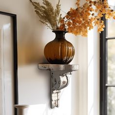 a brown vase sitting on top of a shelf next to a window