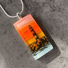 an orange and yellow glass pendant with a lighthouse on the beach in the distance, sitting on carpeted area