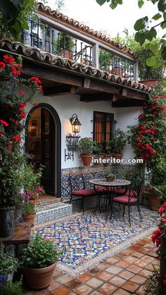 an outdoor dining area with potted plants and flowers on the patio, in front of a spanish style house