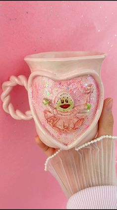 a hand holding a white cup with pink glitters and a frog on the inside