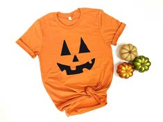 an orange t - shirt with a jack o lantern face on it next to pumpkins