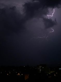 a lightning bolt is seen in the sky over a city at night with dark clouds