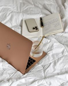 an open laptop computer sitting on top of a bed next to a notebook and pen