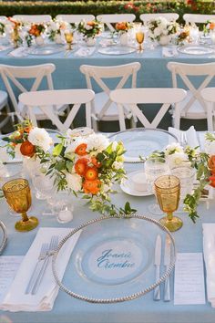 the table is set with white and orange floral centerpieces, gold rimmed glasses, and silverware