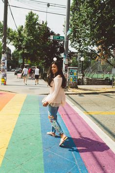 a woman standing in the middle of a rainbow painted street